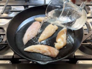 Chicken submerged in water in a skillet