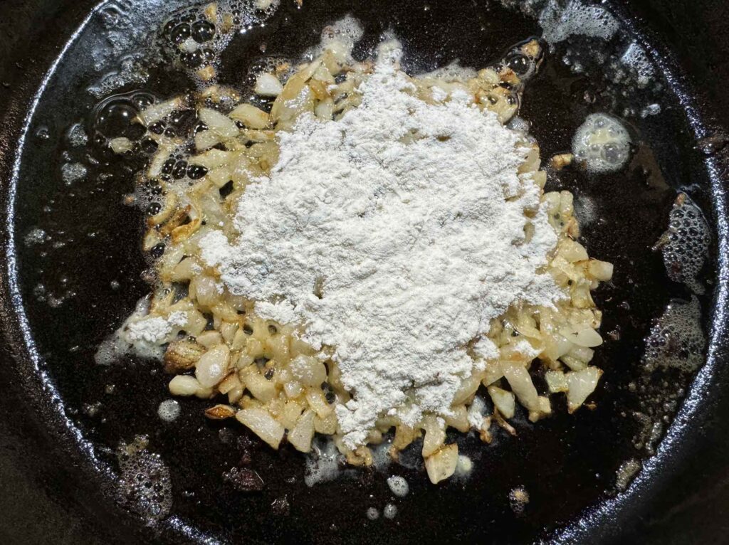 Adding flour to onions and garlic.