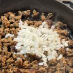Adding onions to the browned meat in a skillet