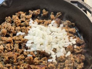 Adding onions to the browned meat in a skillet