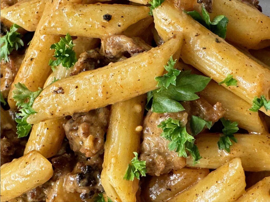 Closeup of creamy sausage pasta with penne, browned sausage, and parsley