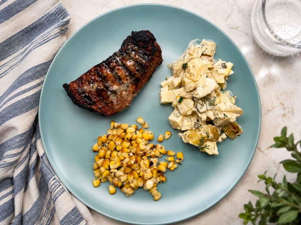 Potato salad on plate with steak and roasted corn