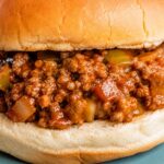 A sloppy joe on a bun resting on a plate blue