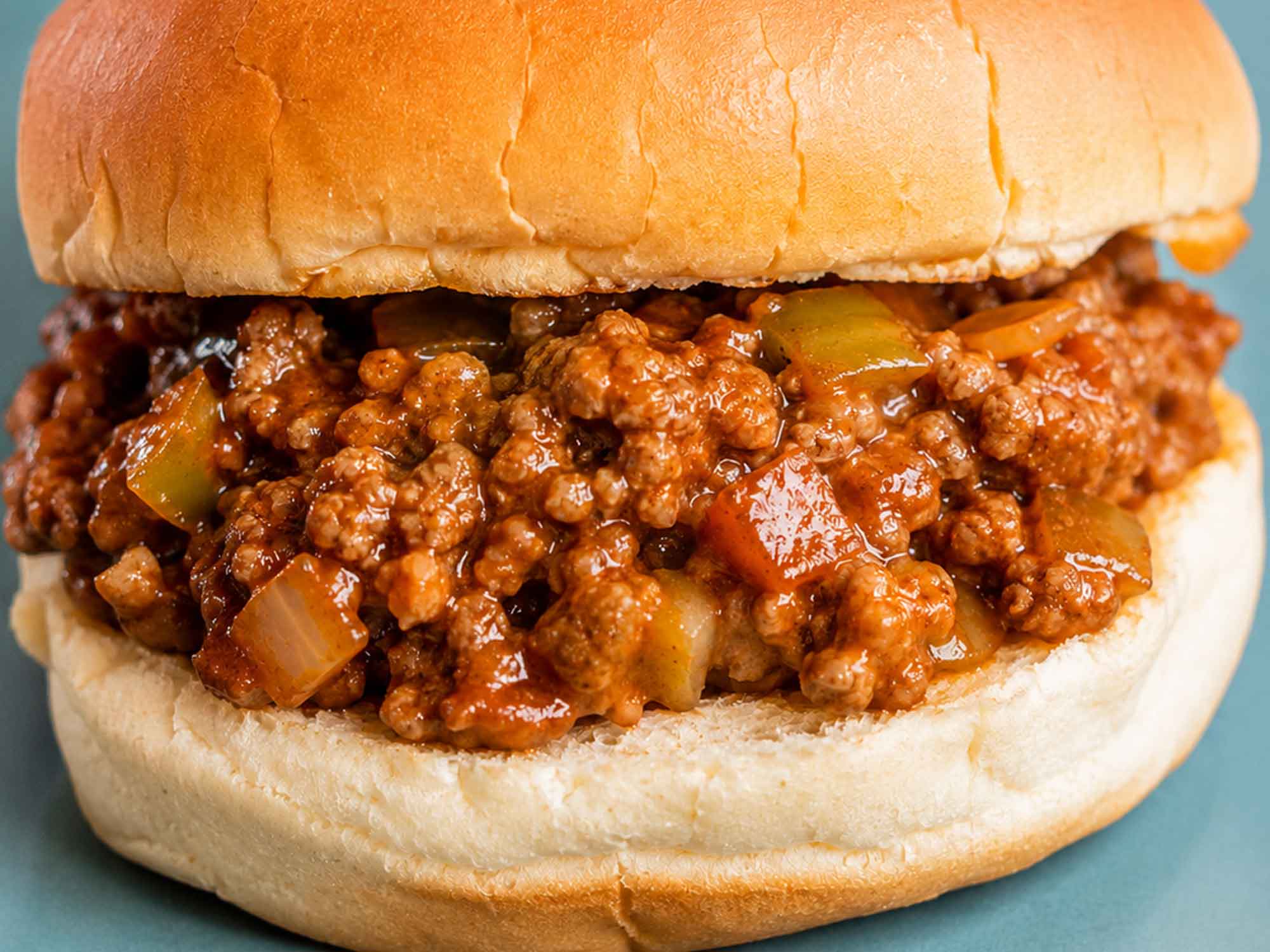 A sloppy joe on a bun resting on a plate blue