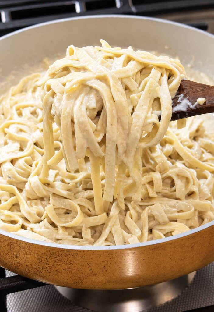 Creamy alfredo sauce coating fettucine on a wooden spoon