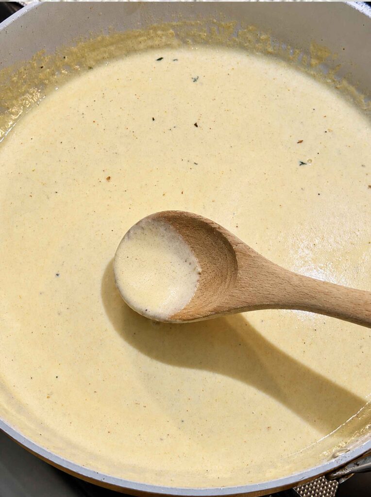 Creamy alfredo sauce with a wooden spoon in a skillet