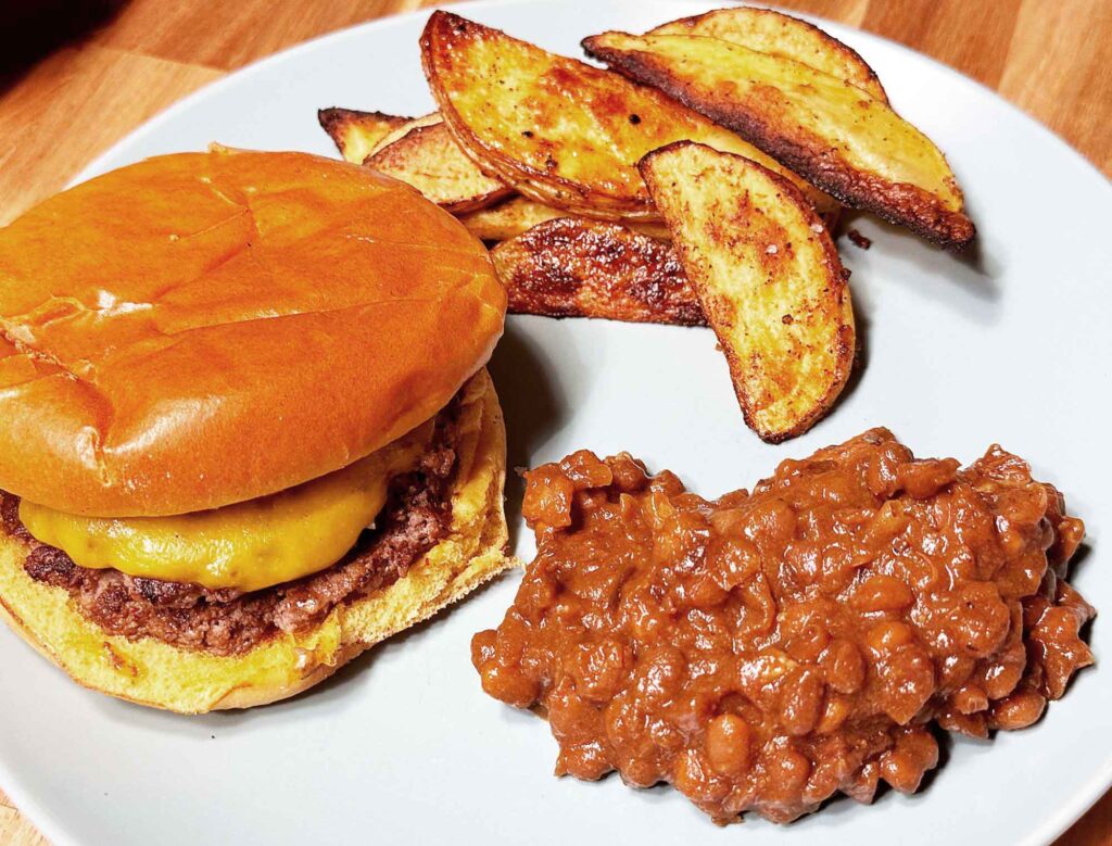 Baked beans on a plate with a burger and oven fries