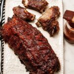 A platter with a full rack of bbq ribs and several pieces torn off, with the meat falling off the bones