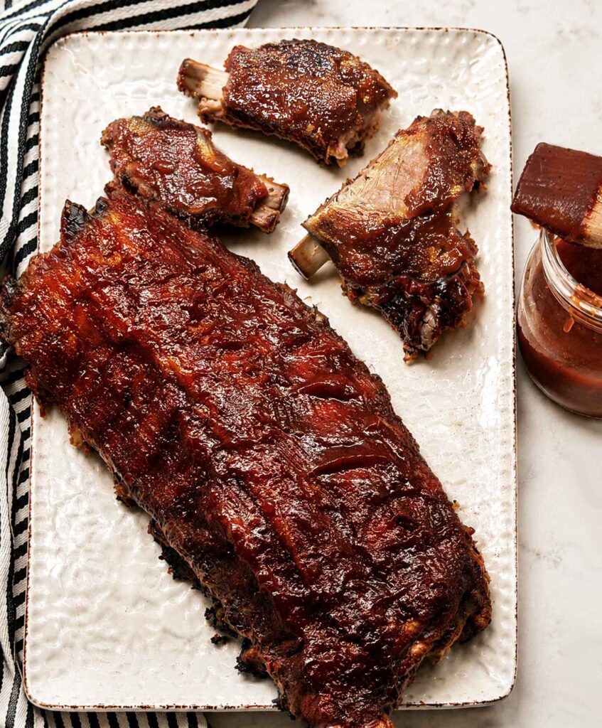 A platter with a full rack of bbq ribs and several pieces torn off, with the meat falling off the bones