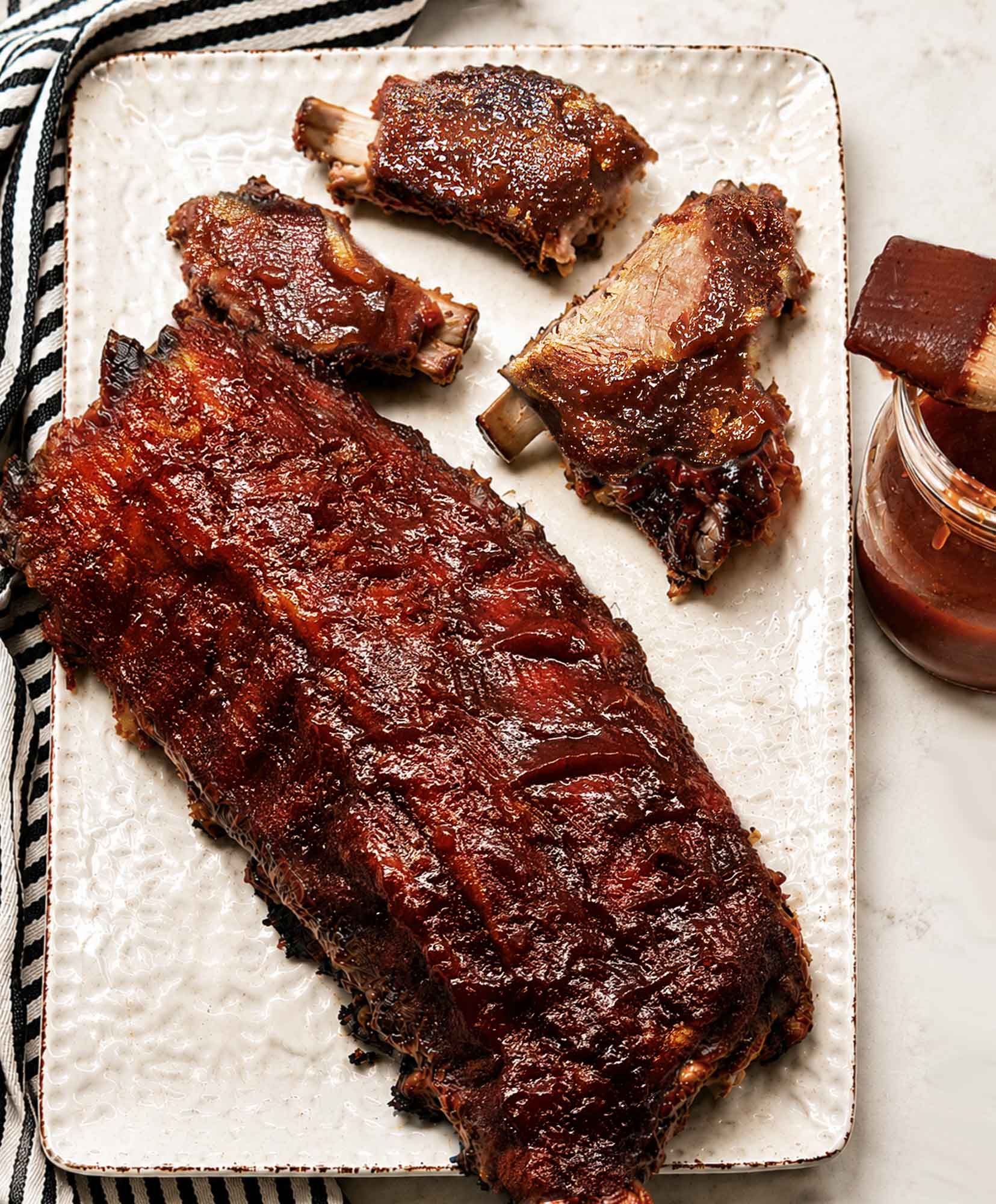 A platter with a full rack of bbq ribs and several pieces torn off, with the meat falling off the bones
