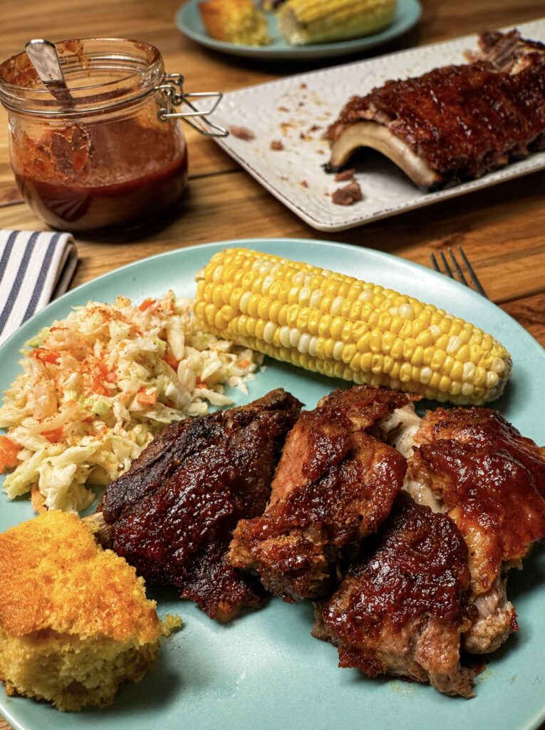 Eating dinner with bbq sauce, ribs, corn on the cob, coleslaw, and cornbread