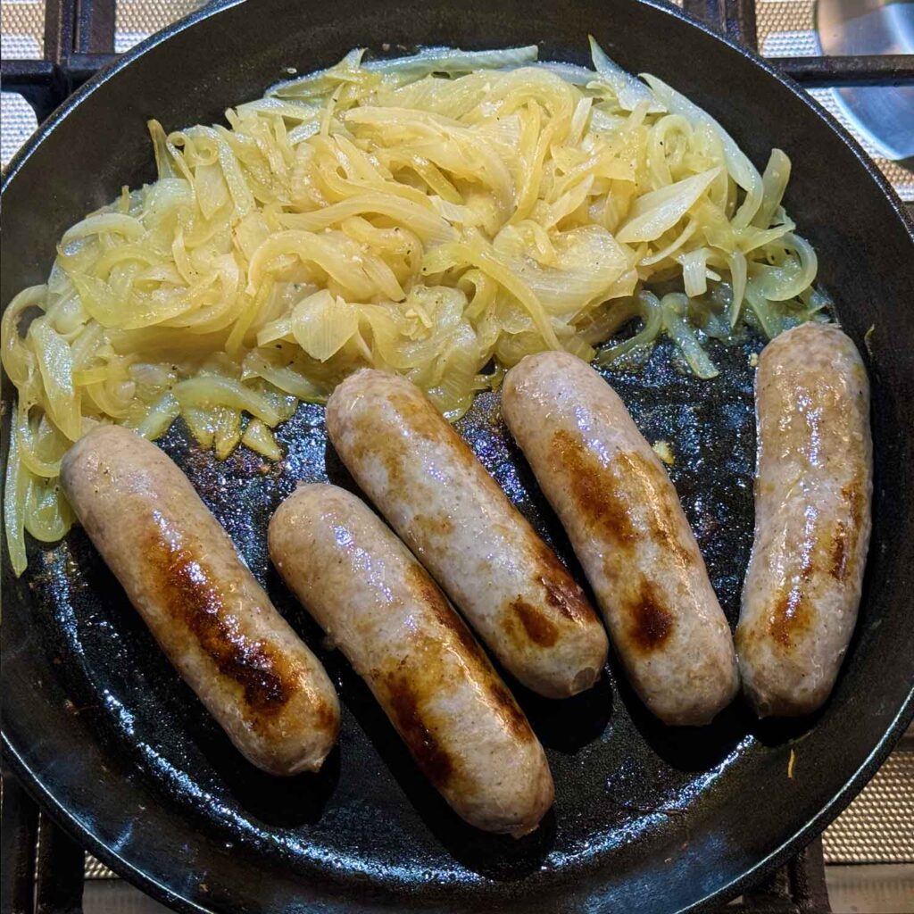 Browning bratwurst in skillet with onions pushed to one side