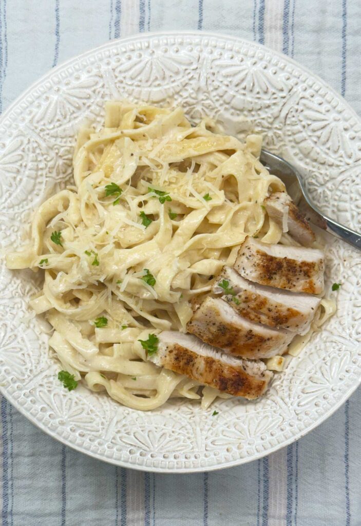 Easy chicken alfredo with homemade sauce, creamy fettuccine topped with sliced seared chicken.