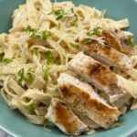 Chicken alfredo with sliced seared chicken over creamy fettucinne in a teal blue bowl, topped with grated Parmesan and parsley