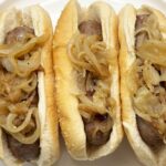 Cooked beer brats with onions in buns on a plate