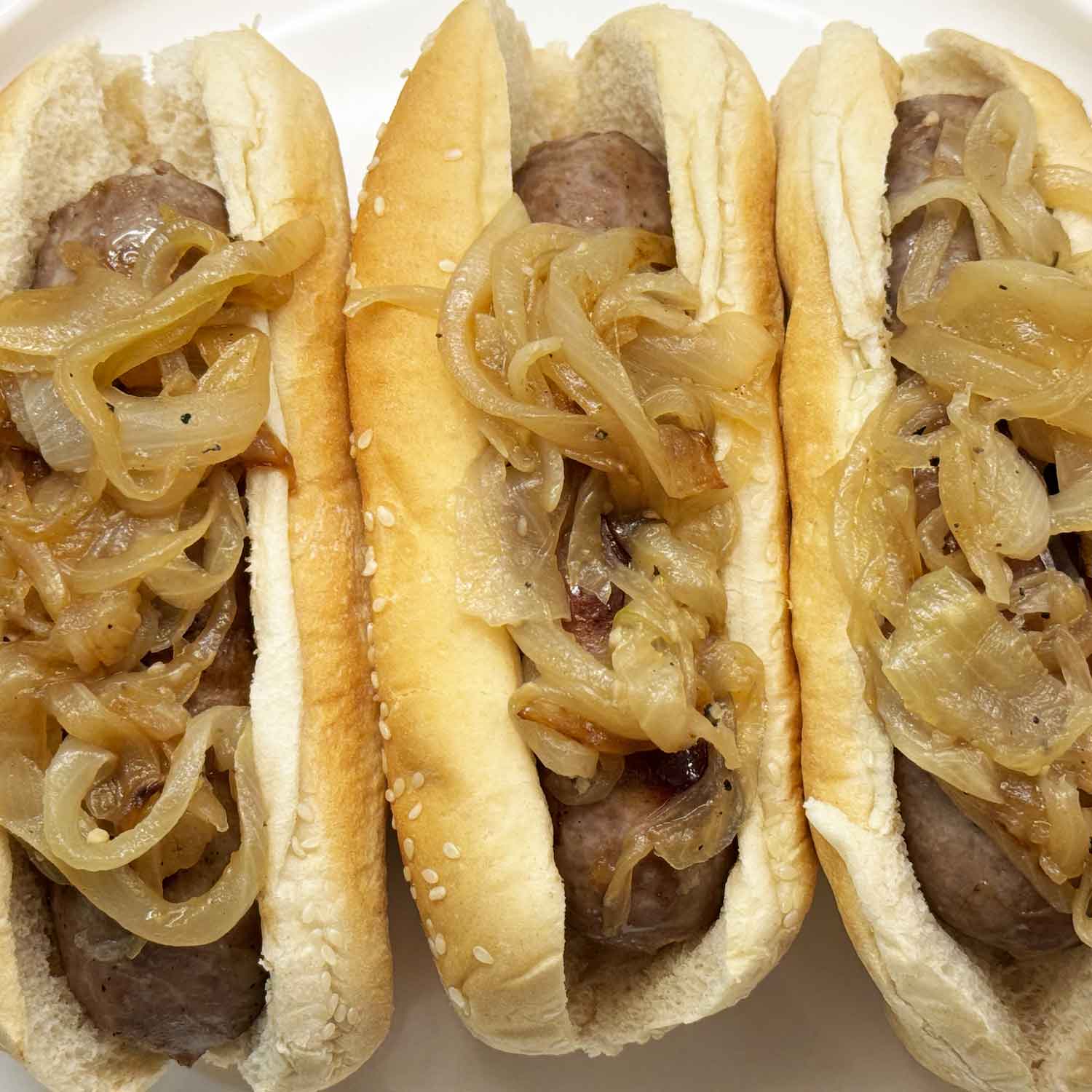 Cooked beer brats with onions in buns on a plate