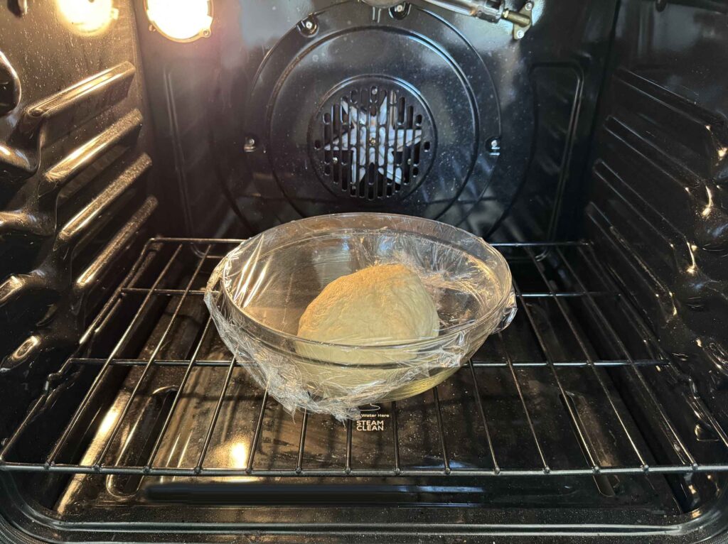 Sourdough cinnamon roll dough covered and in oven with light on