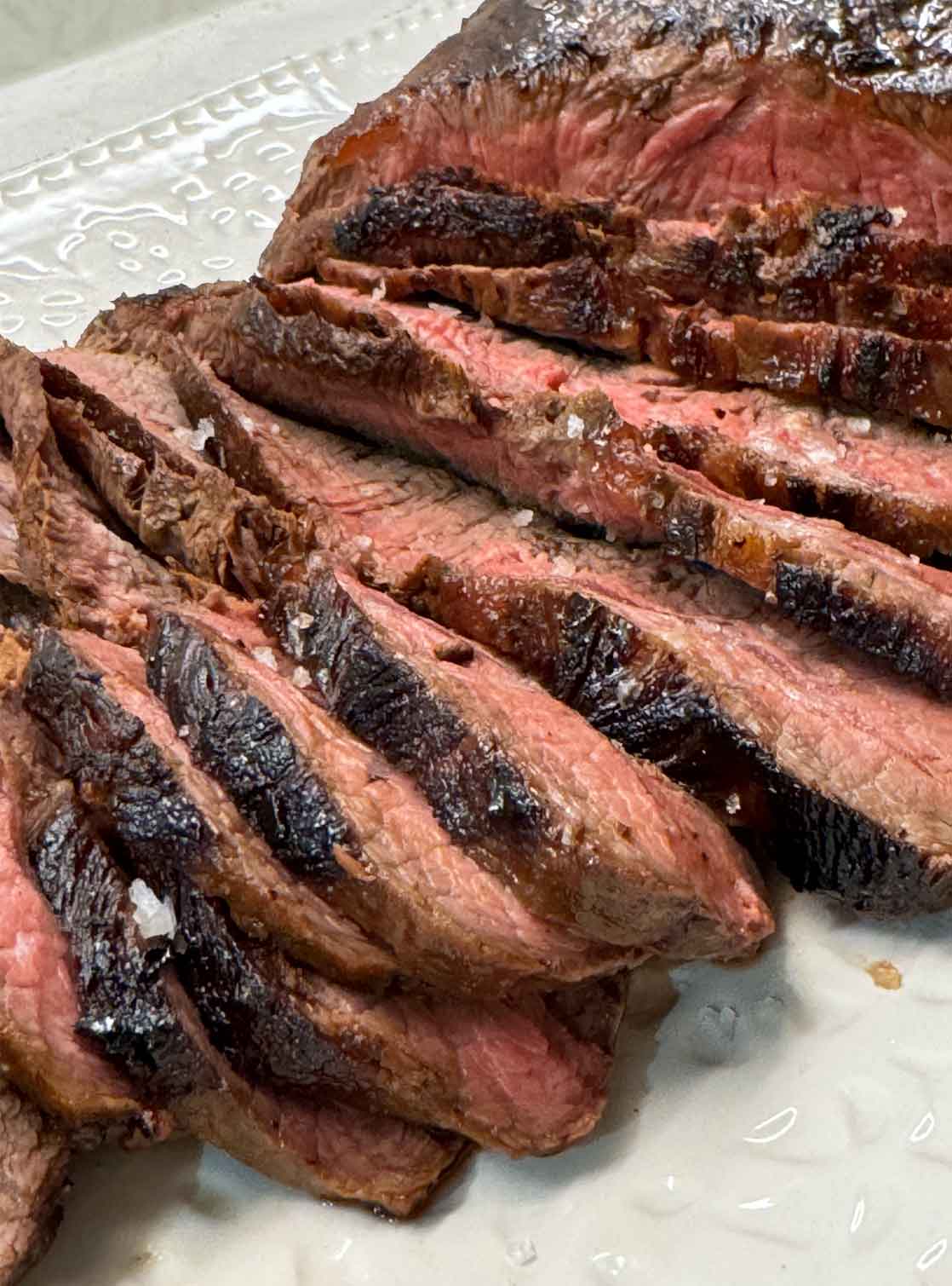 Sliced easy steak marinade flat iron steak fanned on a white platter, showing a juicy pink medium interior and seared crust.