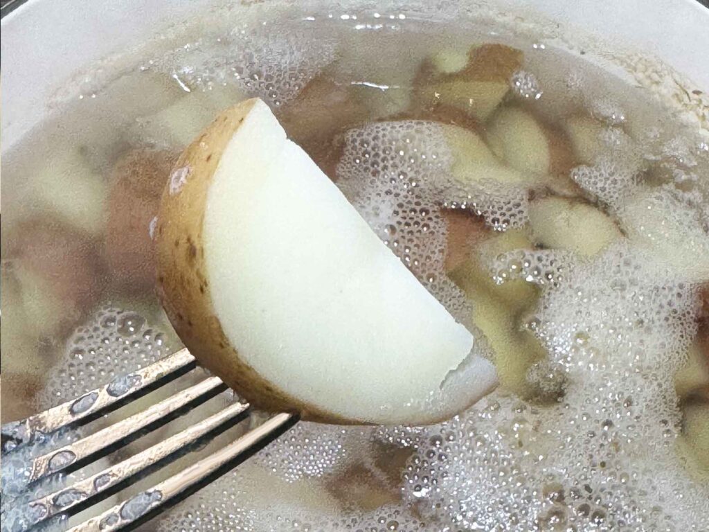 A tender potato on a fork over a pot of potatoes
