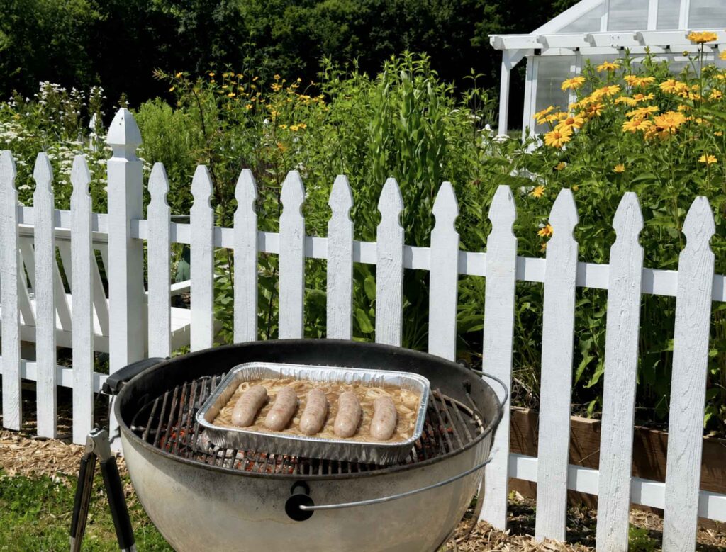 Grilling bratwurst in a foil pan with beer an onions