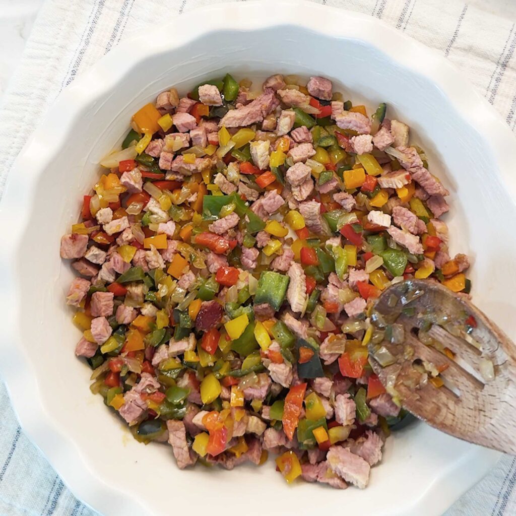 Layering the veggie and meat mixture in the bottom of a 9" pie dish
