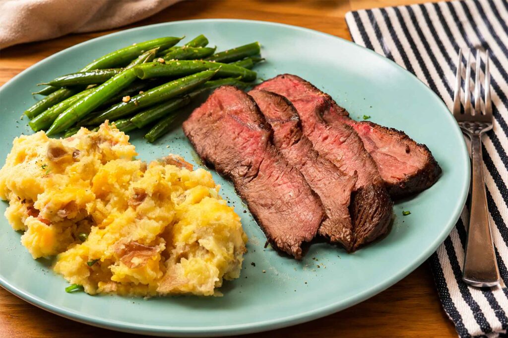 Marinated steak on a blue plate with cheesy mashed potatoes and green beans