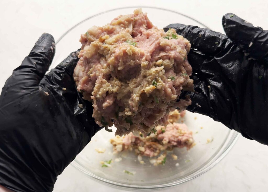 Turkey meatball mixture being mixed with gloved hands