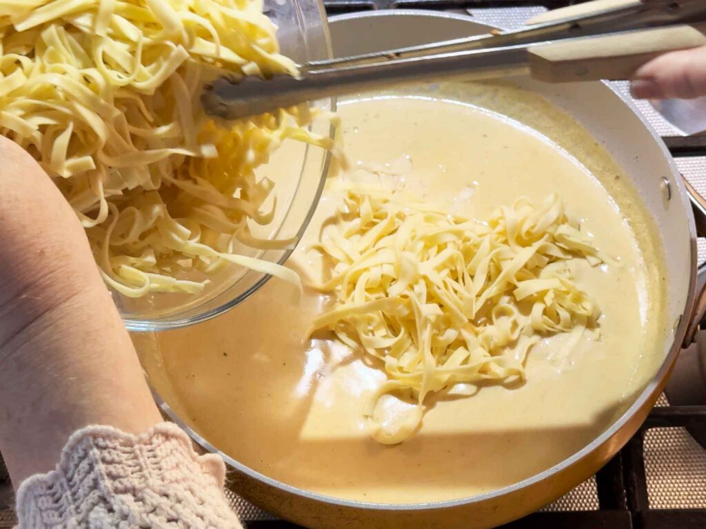 Putting cooked fetuccine pasta into creamy alfredo sauce