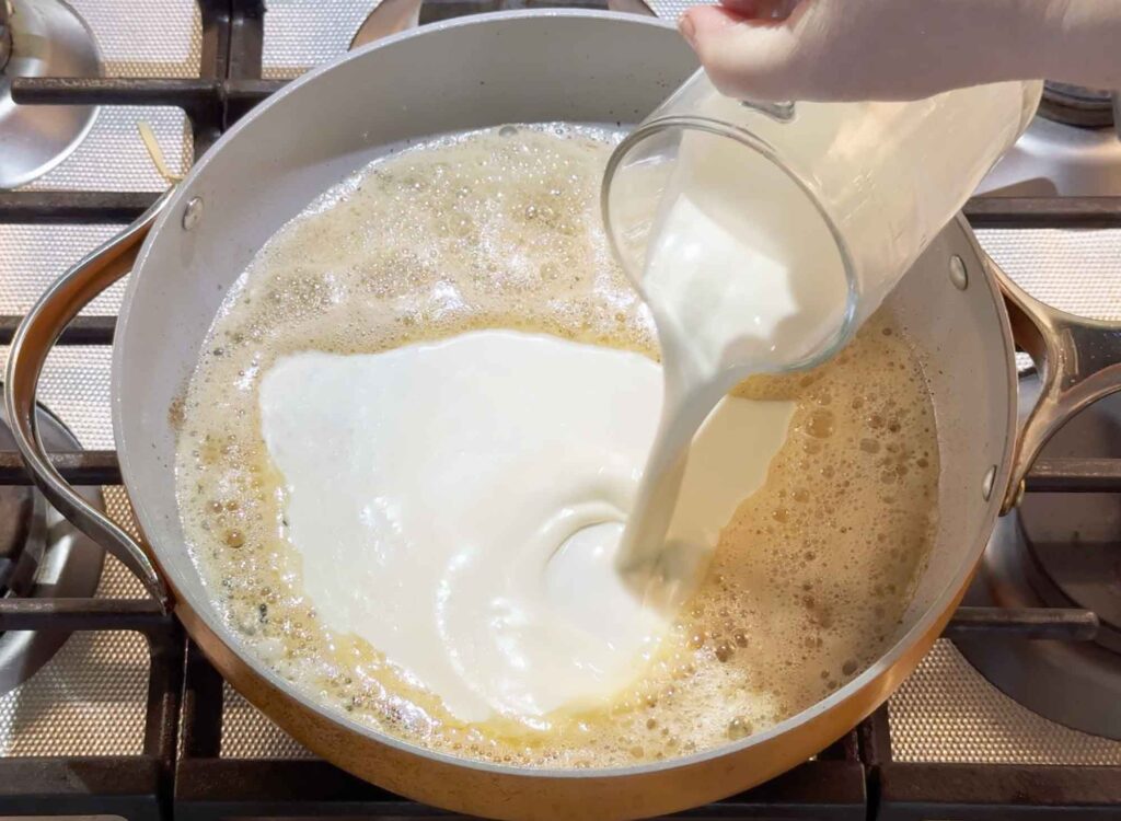 Pouring heavy cream into alfredo sauce in a skillet