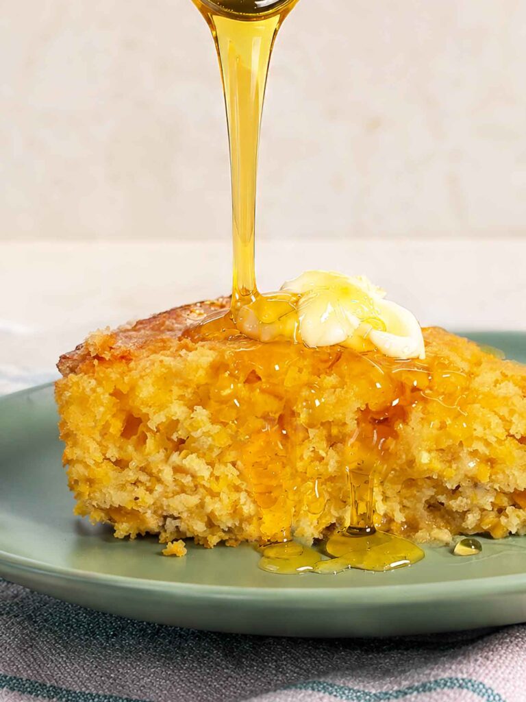 Pouring honey on a piece of cornbread with butter