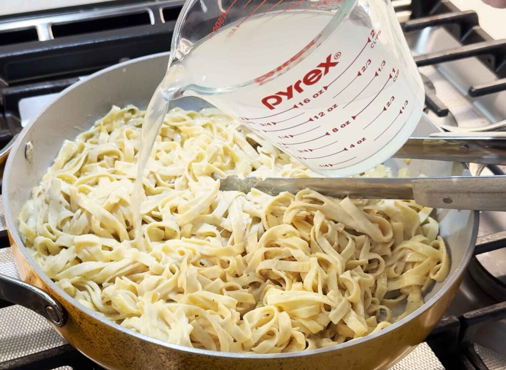 Pour pasta water into the fettucine alfredo in the skillet