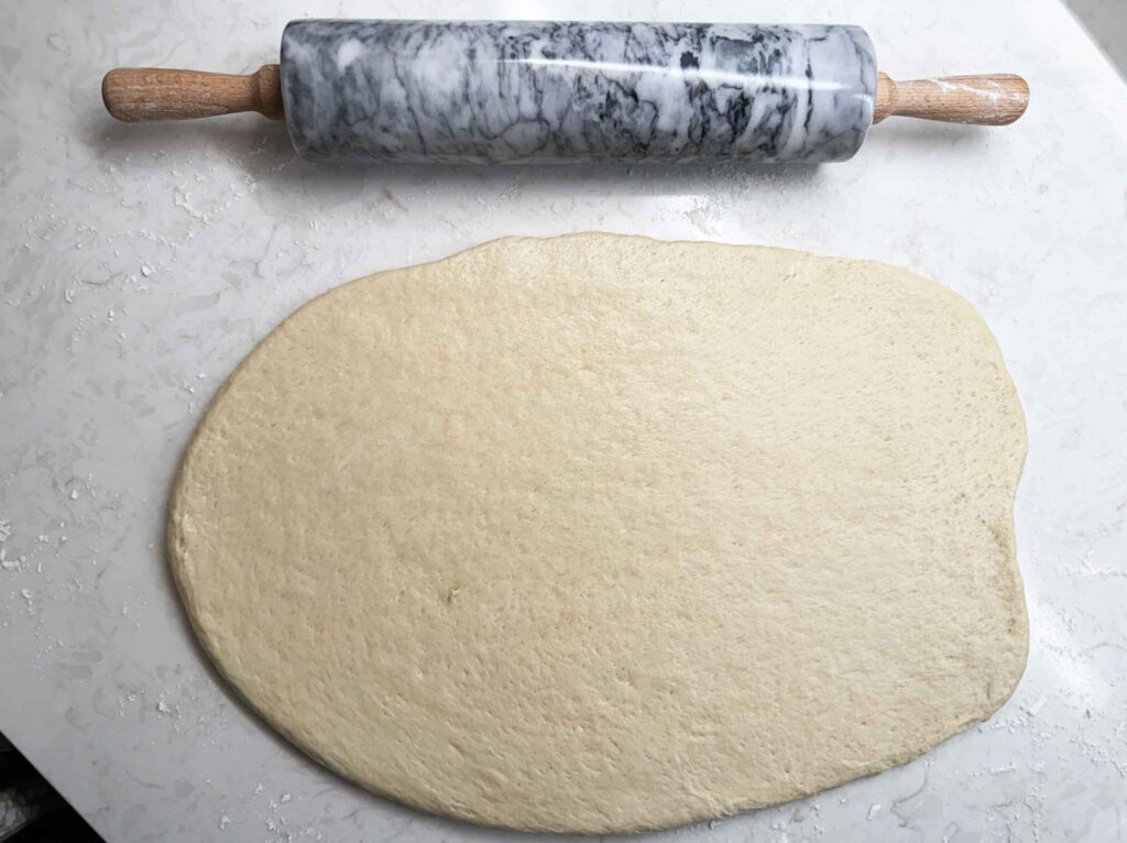 Sourdough cinnamon roll dough rolled out on a floured surface