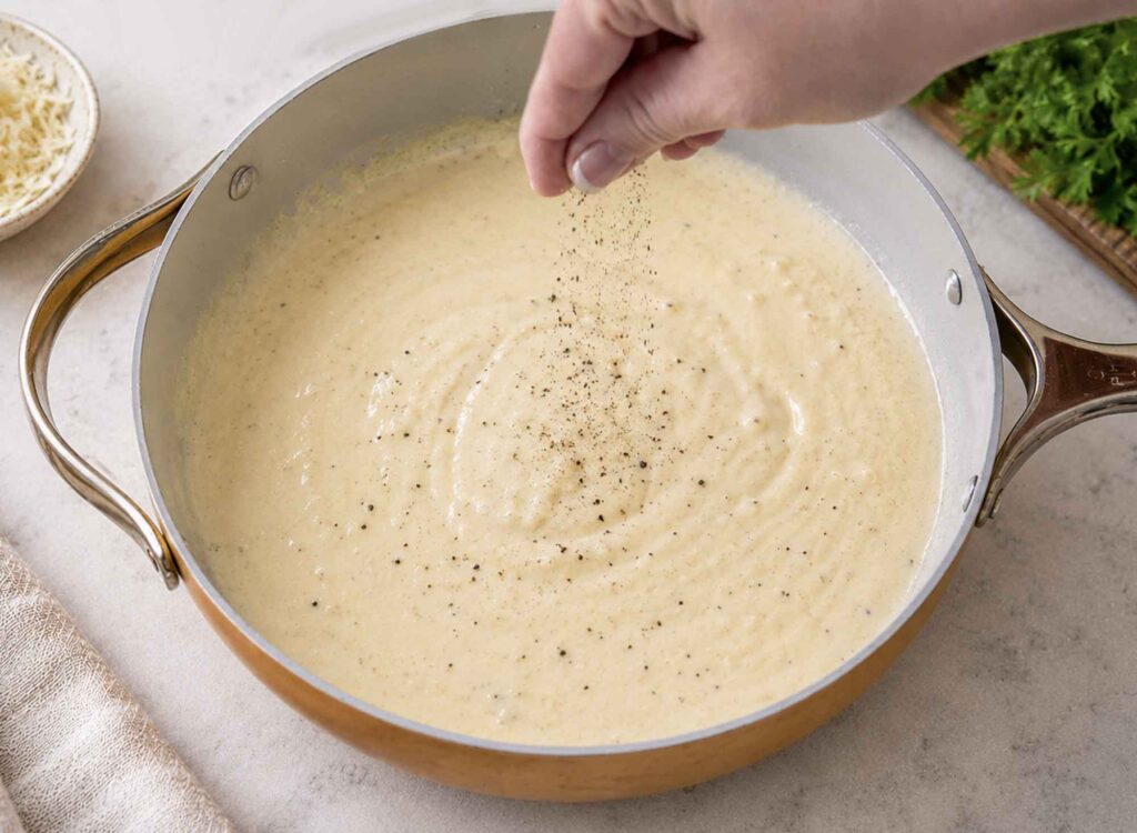 Seasoning homemade Alfredo sauce with pepper