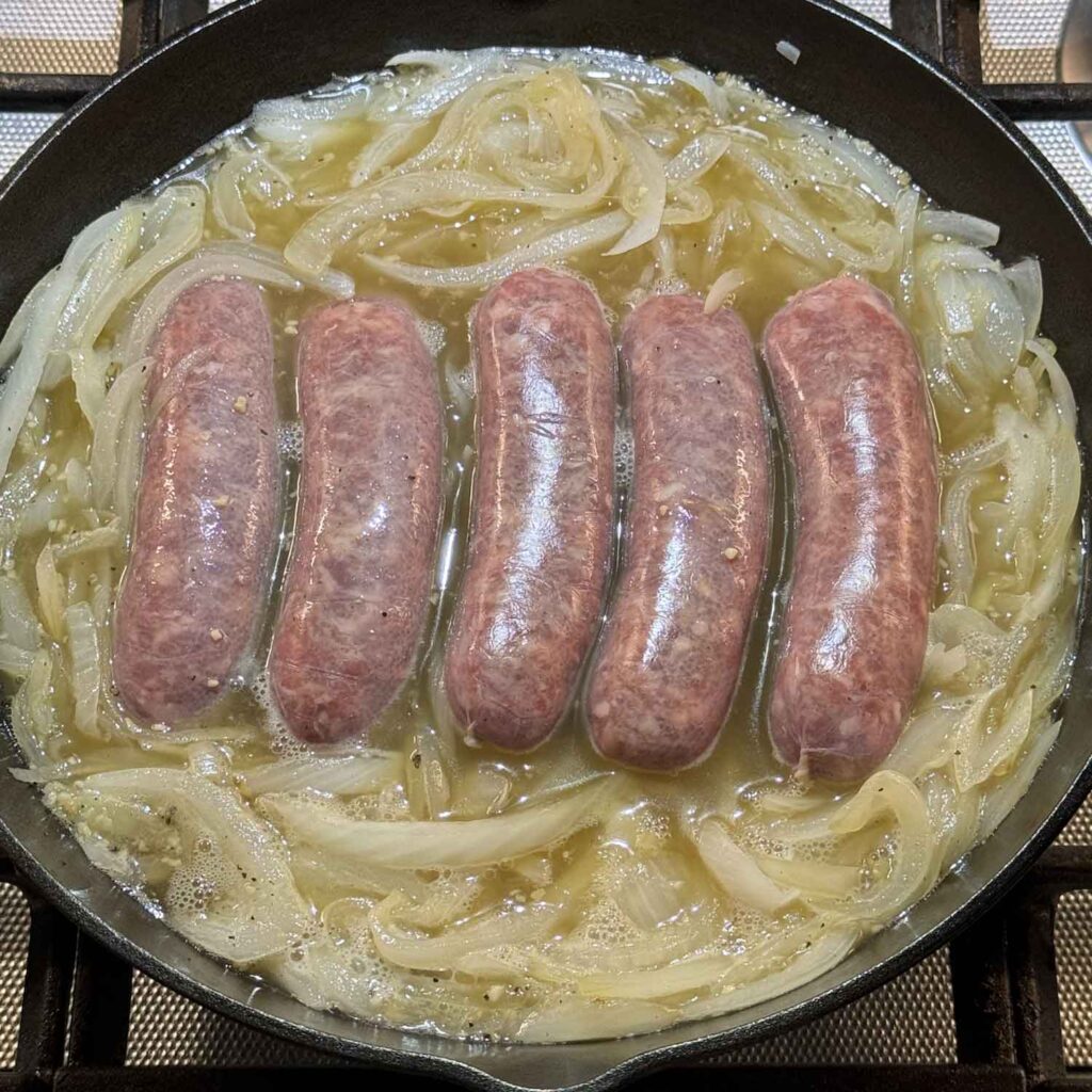 Simmering brats in beer with tiny bubbles around edge of pan