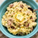 Skin-on mashed potatoes in a blue bowl with melted butter on top