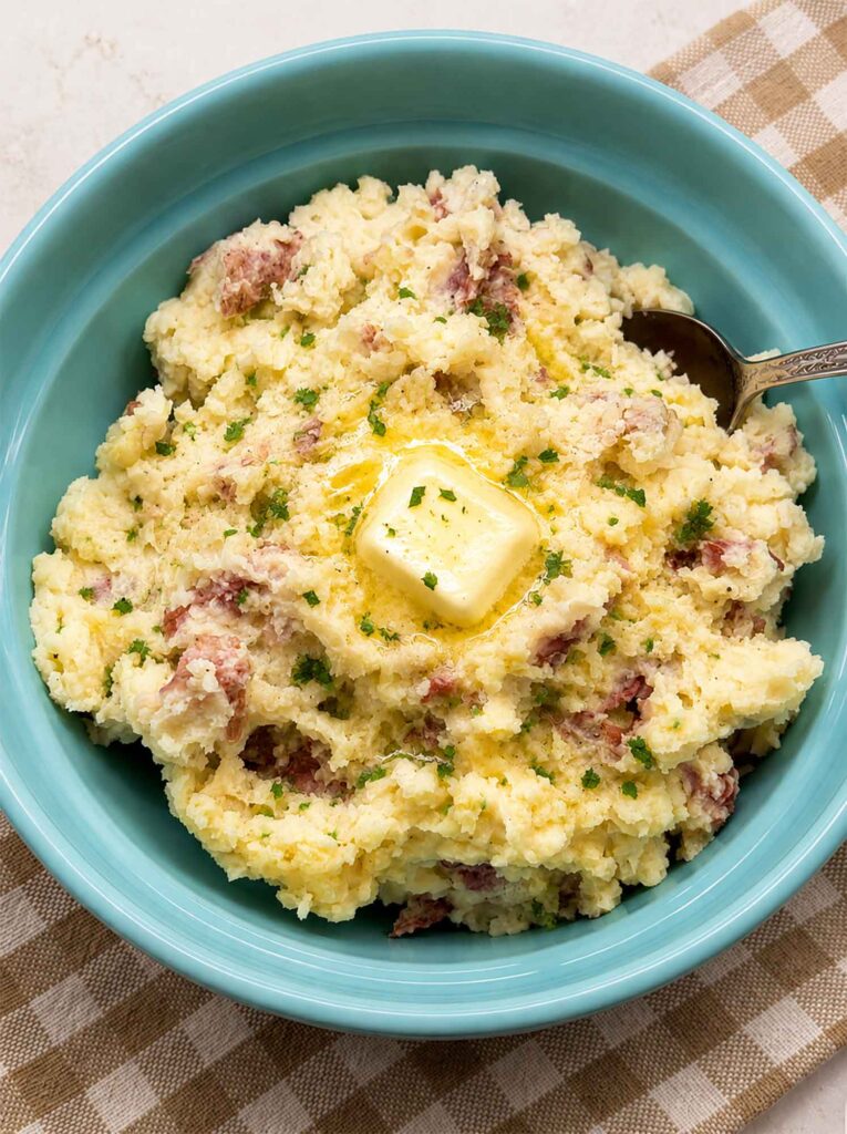 Skin-on mashed potatoes in a blue bowl with melted butter on top