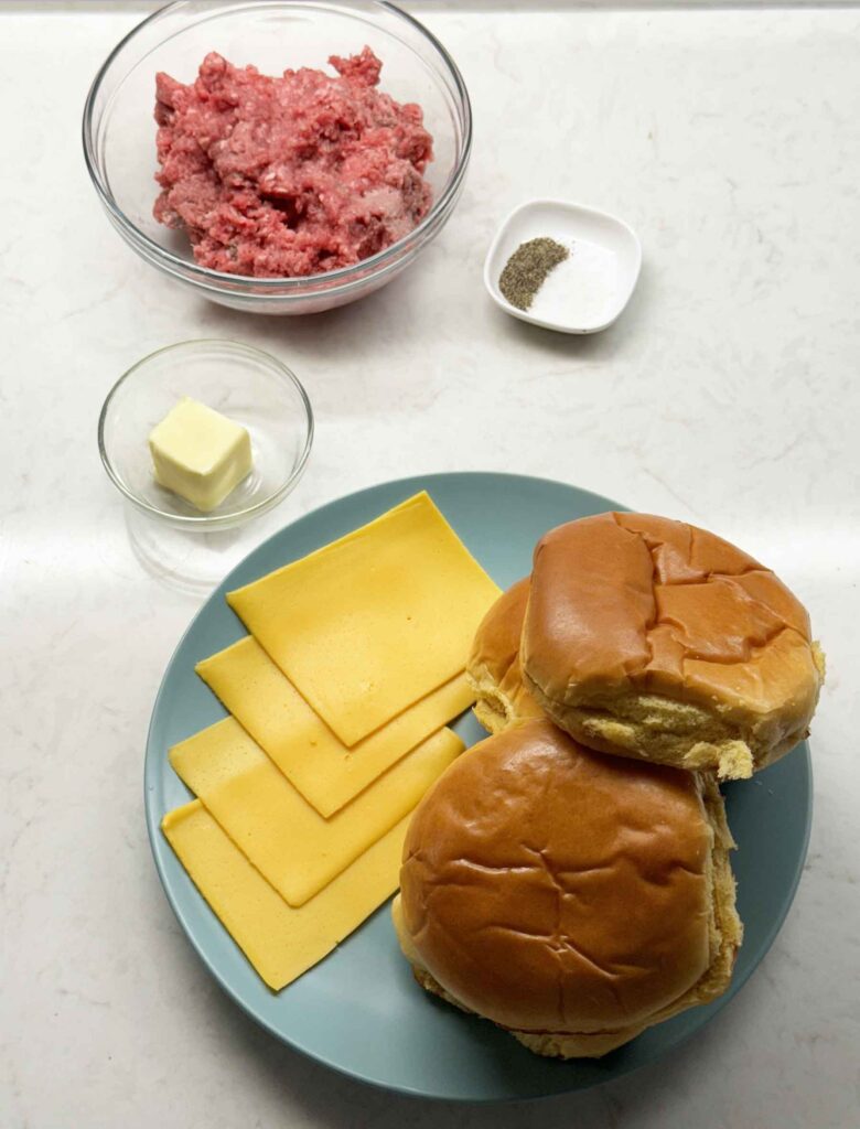 Bowl of ground meat, butter, salt, pepper, American cheese, and brioche buns ready to make smash burgers
