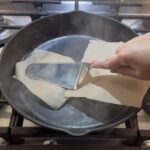 Pressing on the burgers with a piece of parchment paper covering them.