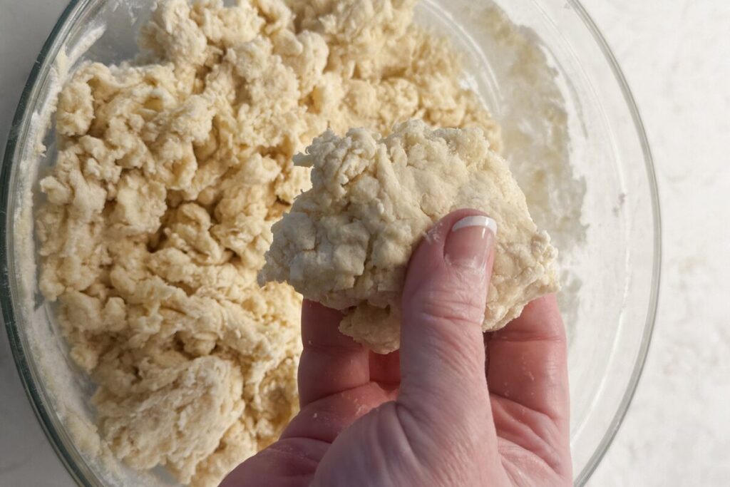A hand squeezing some sourdough discard biscuit batter to make sure it holds together