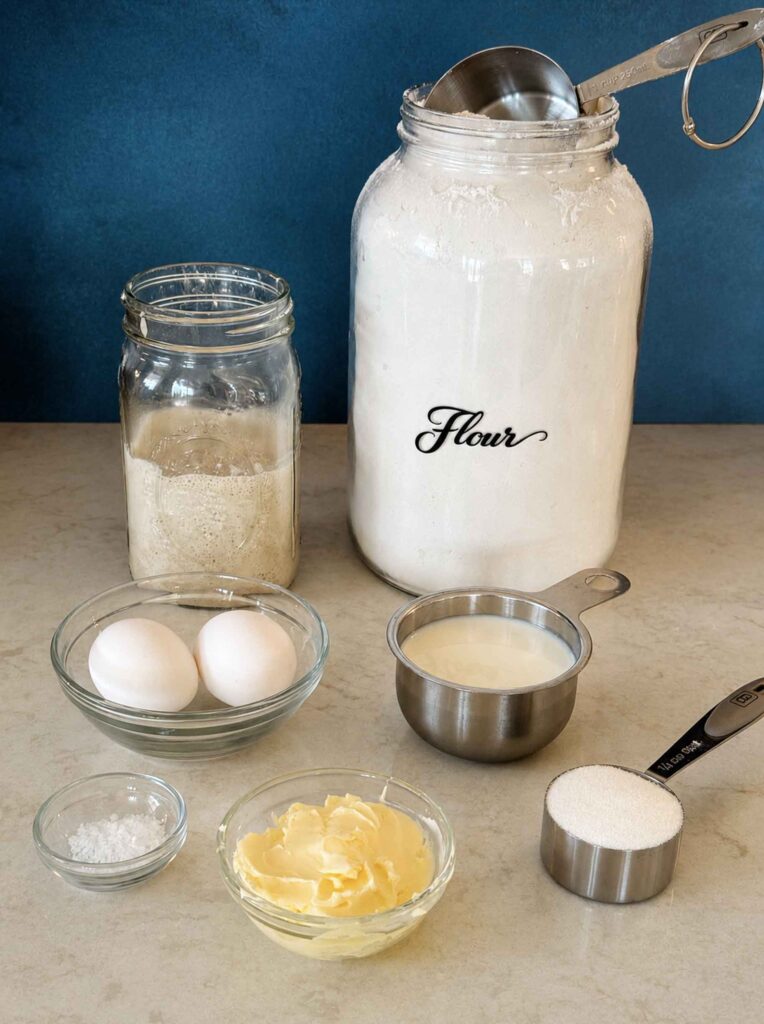 Ingredients to make sourdough cinnamon roll dough: starter, flour, eggs, salt, butter, milk, and sugar