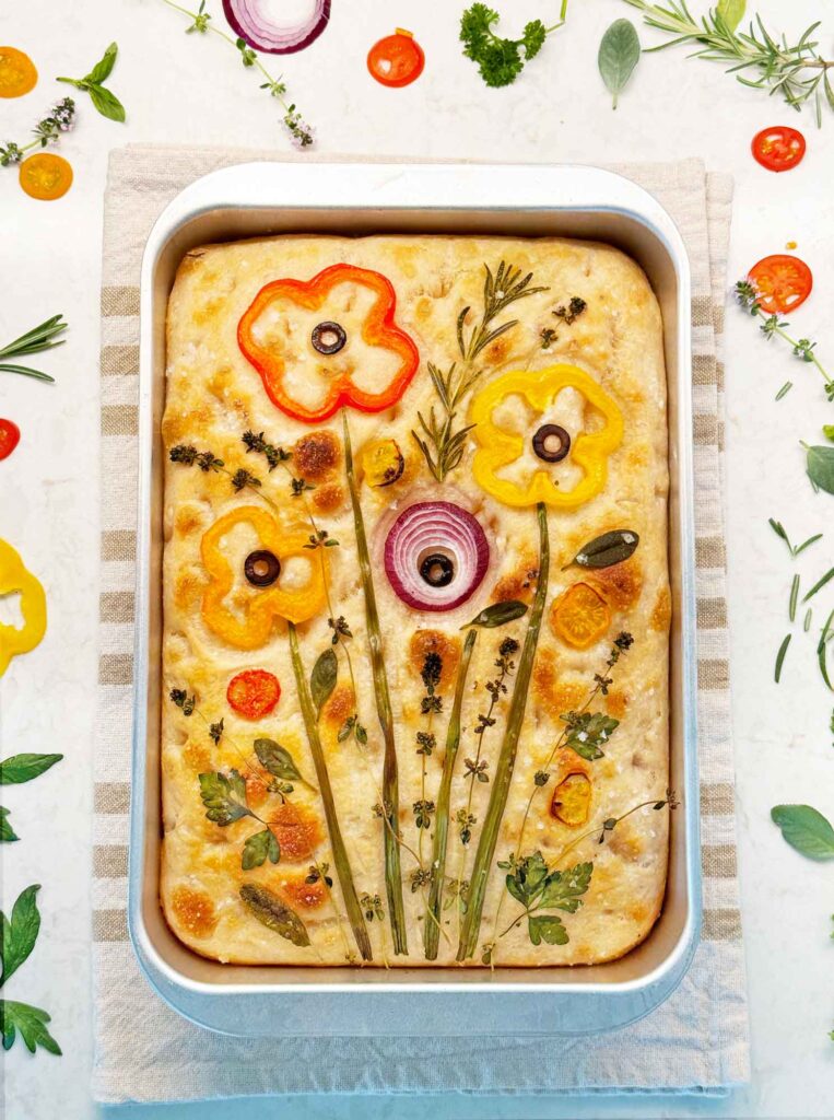 Decorated sourdough focaccia art with wildflowers made from vegetables and herbs.
