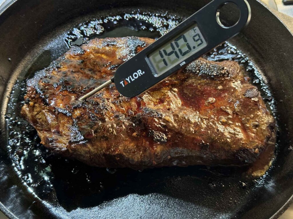 An instant read thermometer that reads 140 F inserted into the thick end of a seared steak
