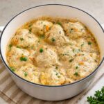 Fluffy dumplings steamed on top of the chicken stew in a white pot, puffed up and cooked through