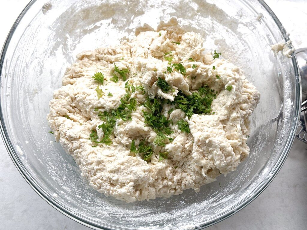 Soft, sticky sour cream dumpling dough in a wood bowl with fresh chopped parsley folded in