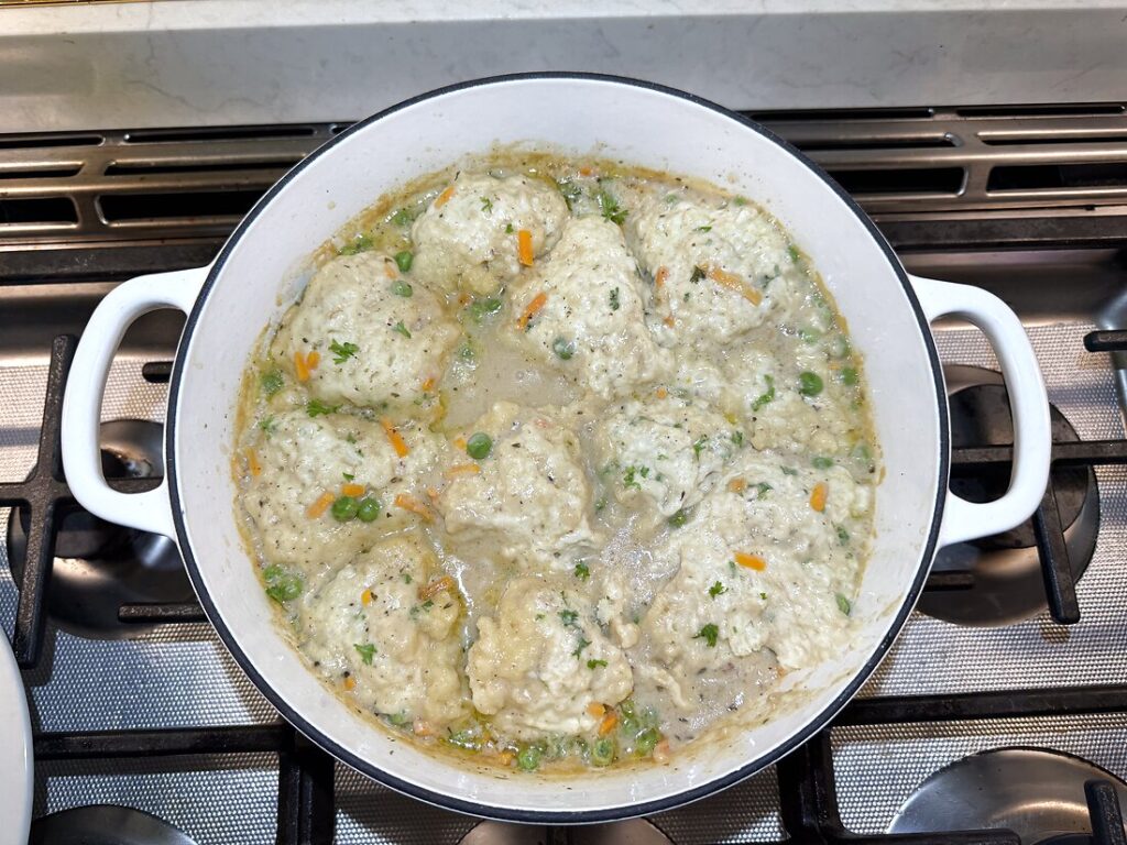 Fluffy dumplings steamed on top of the chicken stew in a white pot, puffed up and cooked through