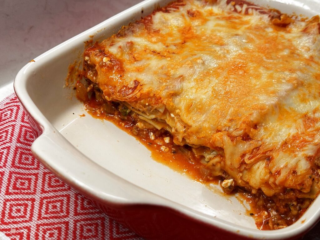 A slice of lasagna lifted to show two layers of noodles, filling, and meat sauce.