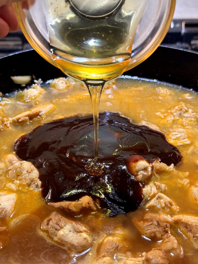 Honey being drizzled over BBQ sauce and broth in the skillet with the chicken and rice.