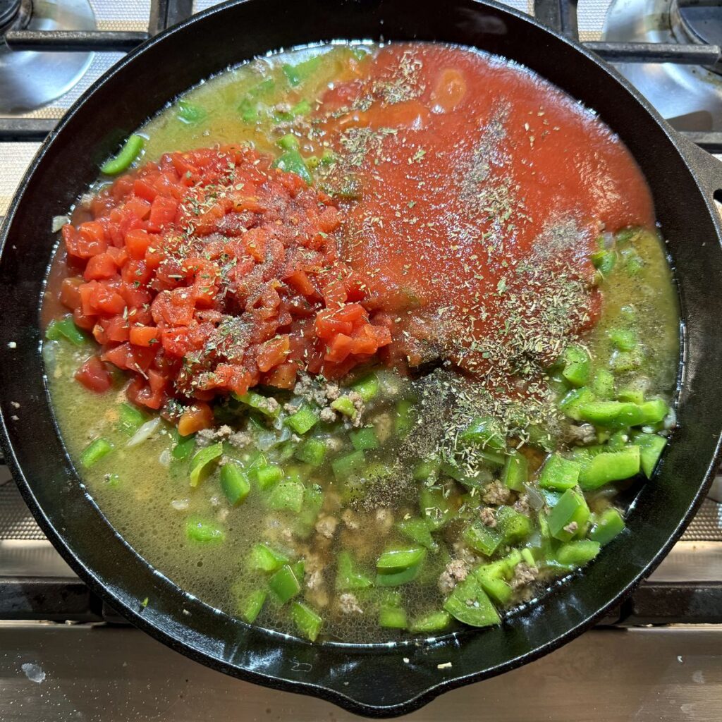 Diced tomatoes, tomato sauce, and seasonings added to the beef and peppers in the skillet.