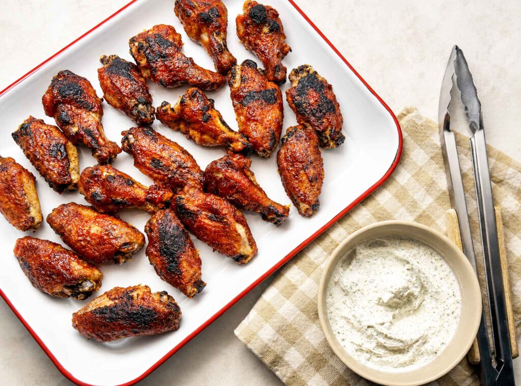 Platter of baked BBQ chicken wings served with a bowl of ranch dip