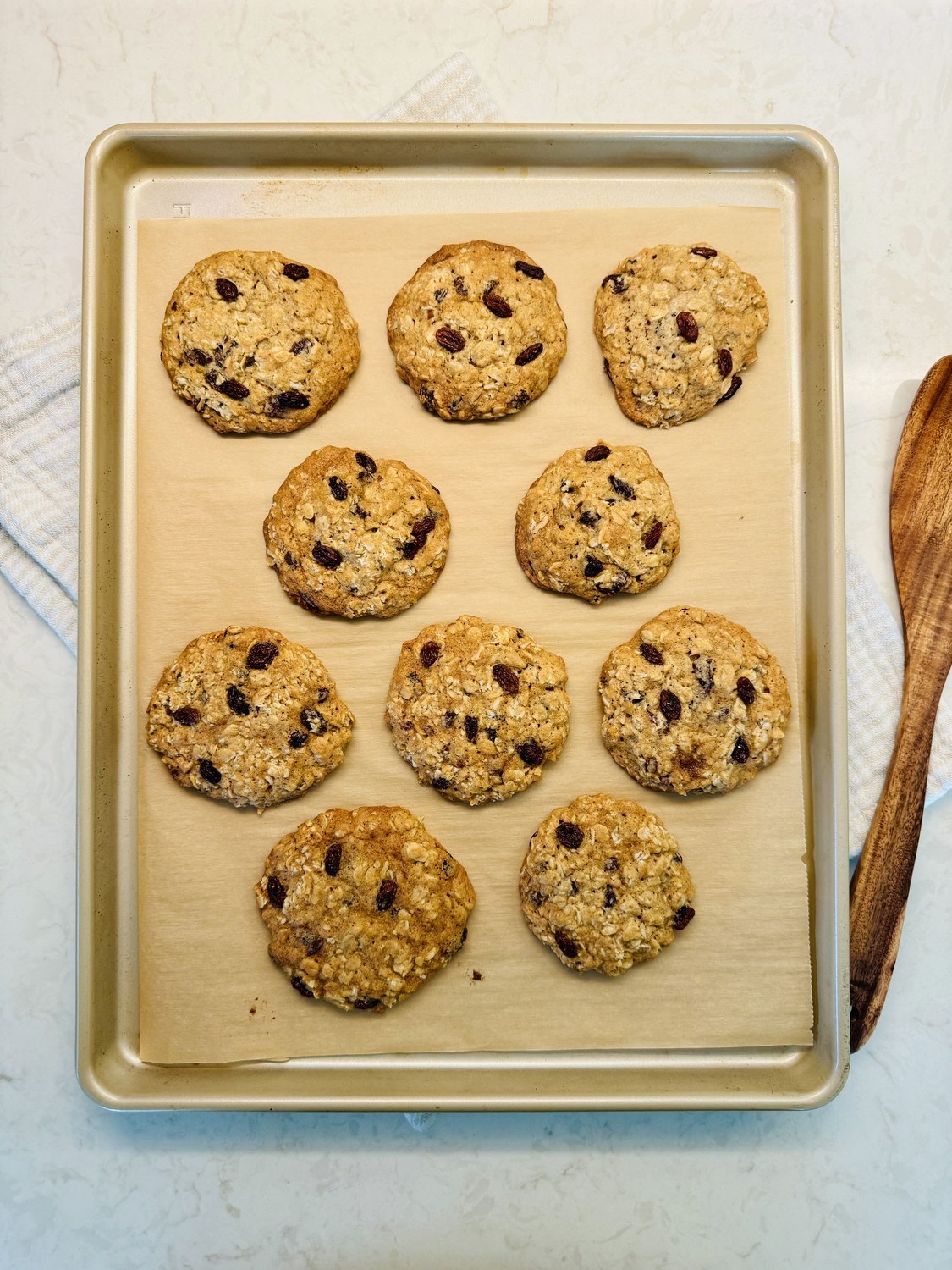Fresh-baked sourdough oatmeal cookies with raisins on a parchment-lined baking sheet.
